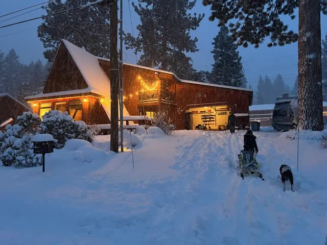 Pulling a sled with the dog toward the snowy cabin at dusk